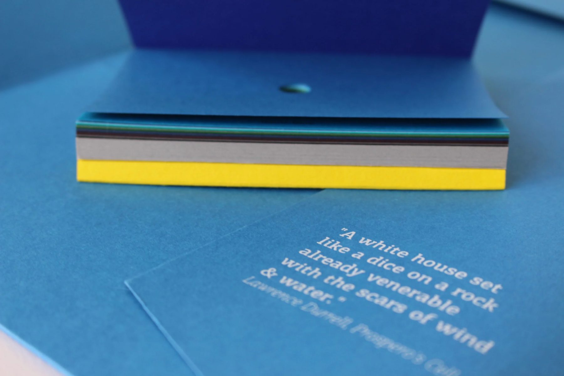 Stack of blue, grey and yellow business cards for The White House in Kalami, Corfu, with a line by Lawrence Durrell, designed by Poua Design