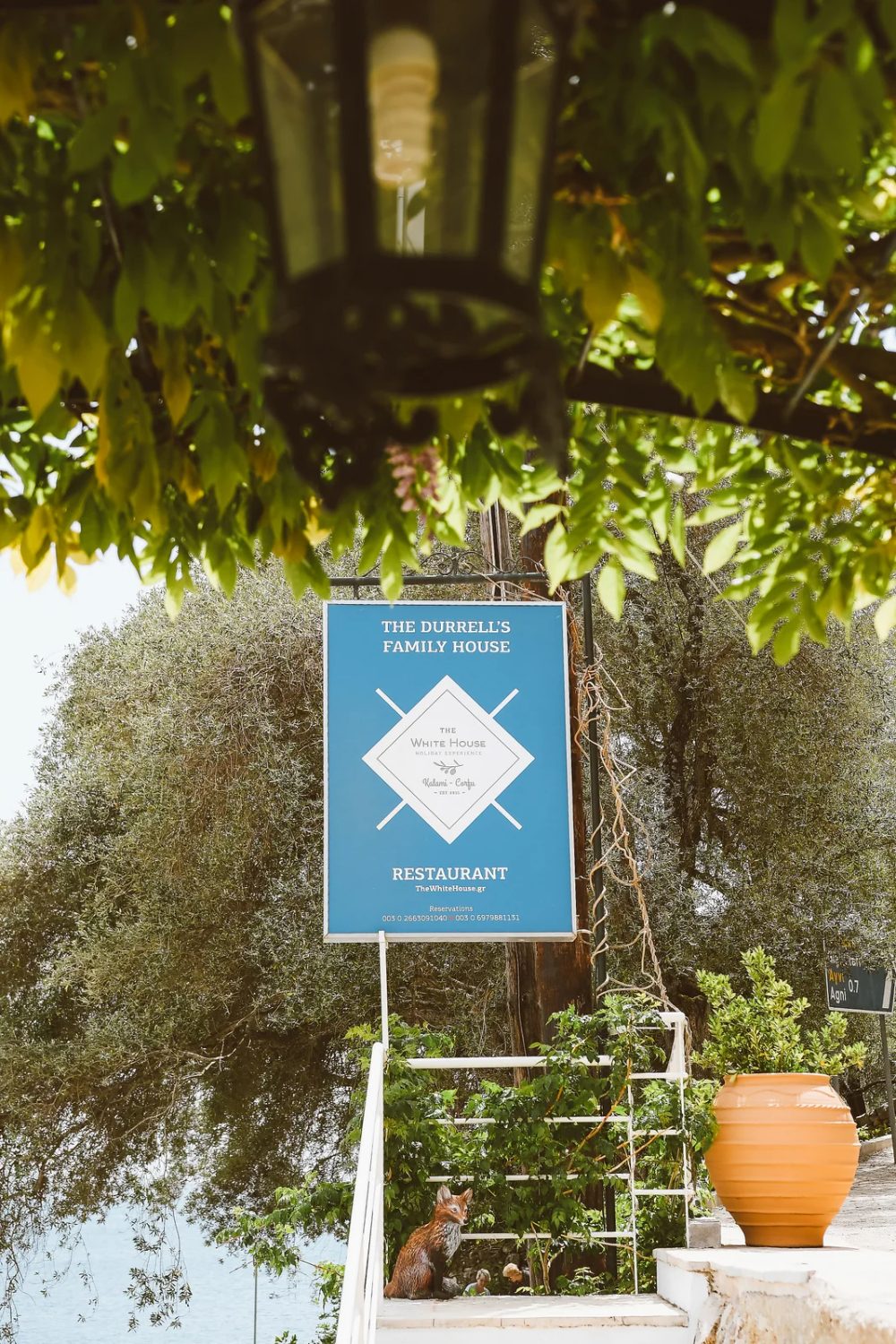 Blue and white sign with the logo of The White House among olive trees in Kalami, Corfu, signage design by Poua Design